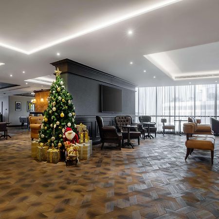 Radisson Blu Hotel, Dubai Canal View Exterior photo The image shows a modern lobby or lounge area decorated for the holiday season. A decorated Christmas tree is prominently displayed, adorned with lights and ornaments, alongside wrapped gifts. The flooring features a patterned tile or brick design, a