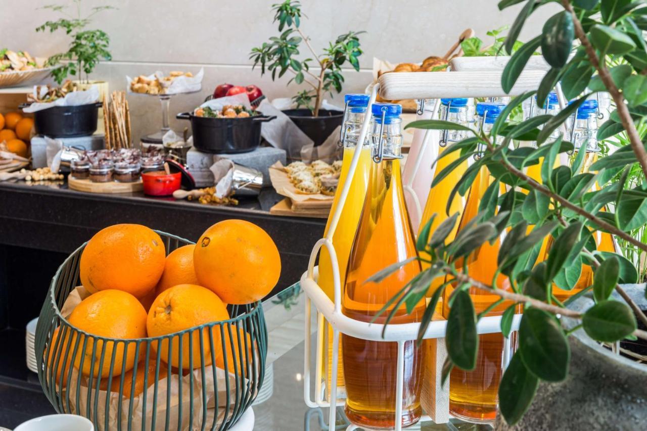 Radisson Blu Hotel, Dubai Canal View Exterior photo The photo shows a buffet-style setup featuring a variety of refreshments and snacks. In the foreground, there is a bowl filled with oranges. Nearby, there's a rack displaying several bottles filled with colorful beverages, likely juices or flavored d