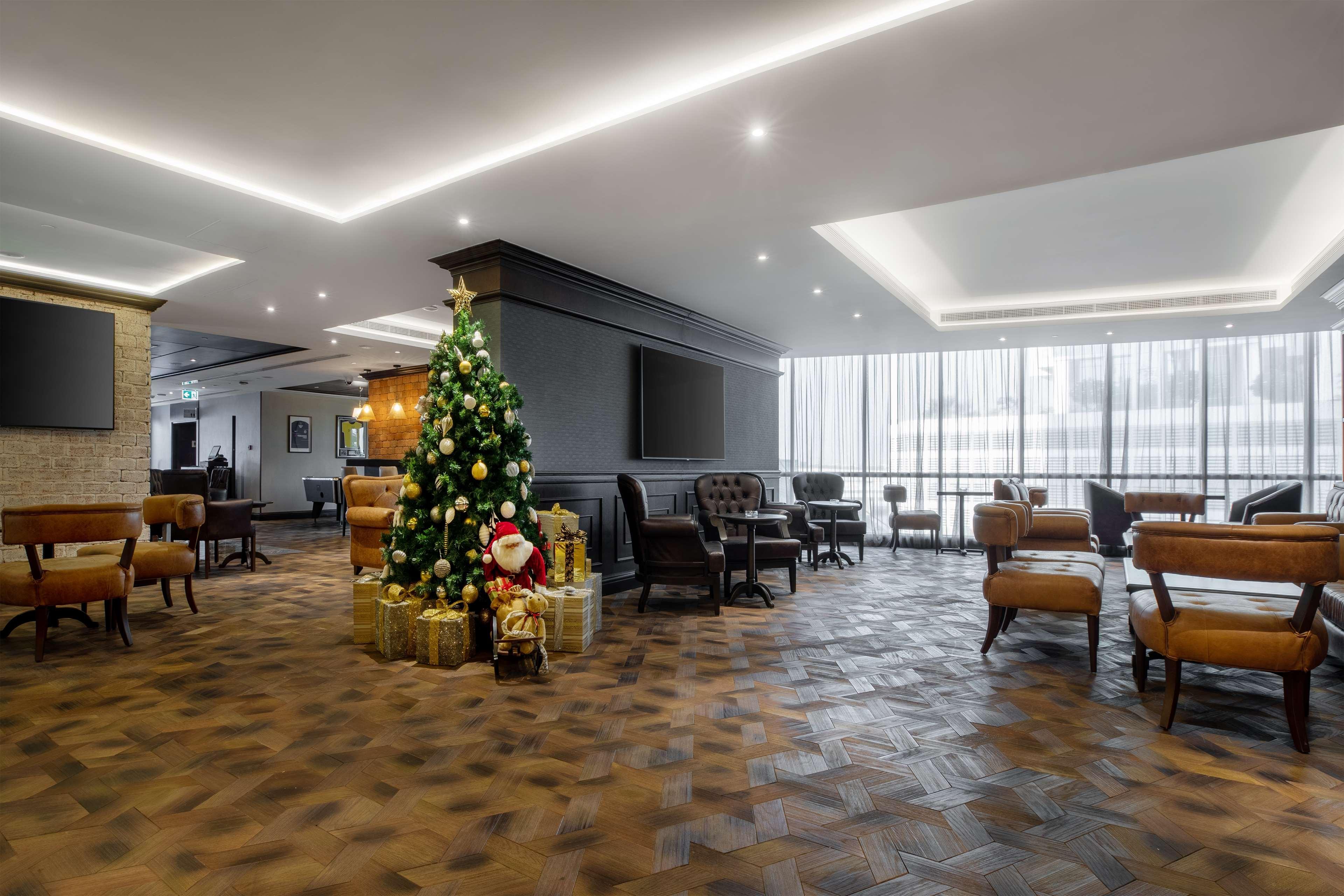 Radisson Blu Hotel, Dubai Canal View Exterior photo The image shows a modern lobby or lounge area decorated for the holiday season. A decorated Christmas tree is prominently displayed, adorned with lights and ornaments, alongside wrapped gifts. The flooring features a patterned tile or brick design, a