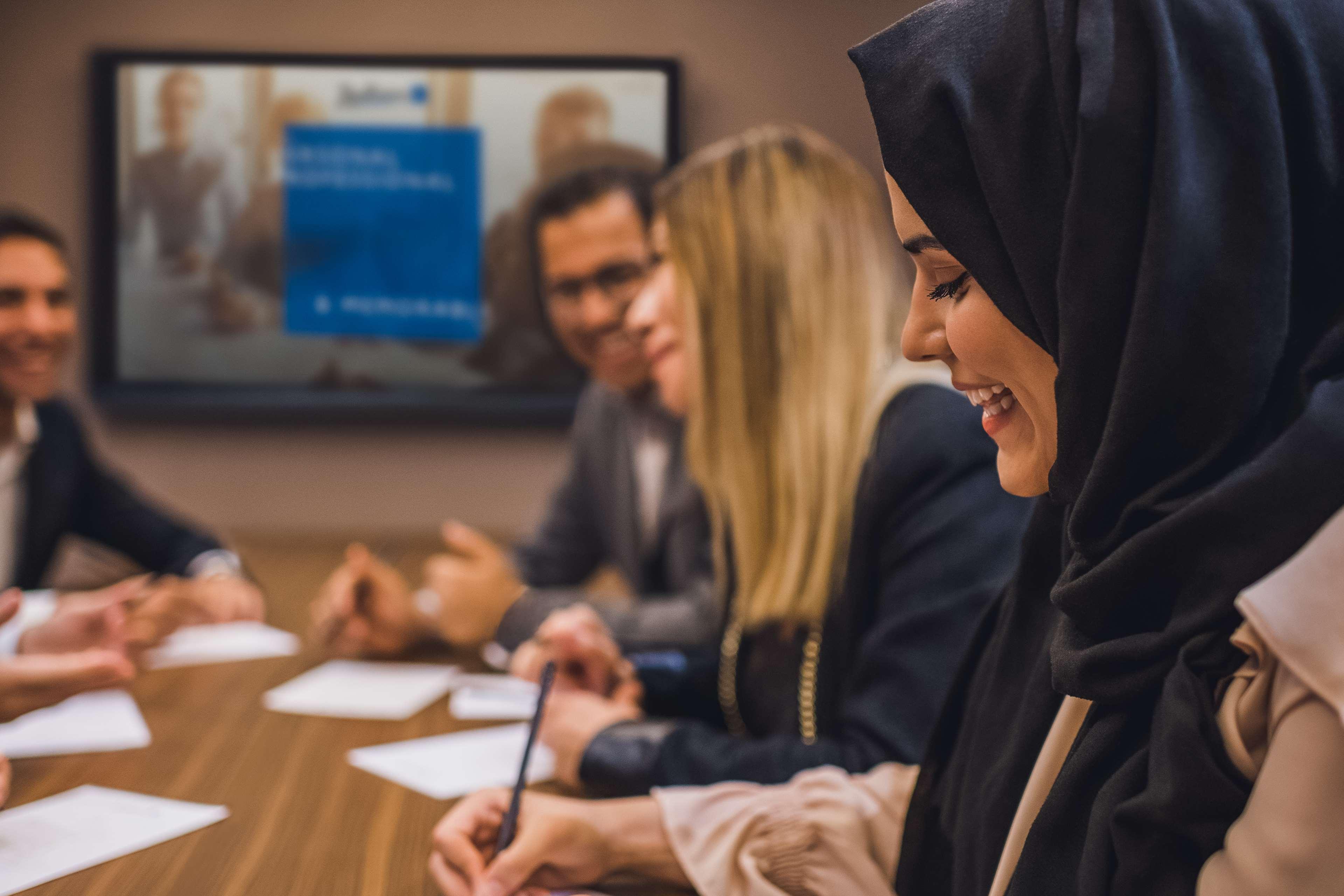 Radisson Blu Hotel, Dubai Canal View Exterior photo The photo shows a business meeting taking place in a conference room. There are several people seated around a wooden table, engaged in discussion. One person is wearing a hijab and is smiling, while others appear to be focused on their notes or disc