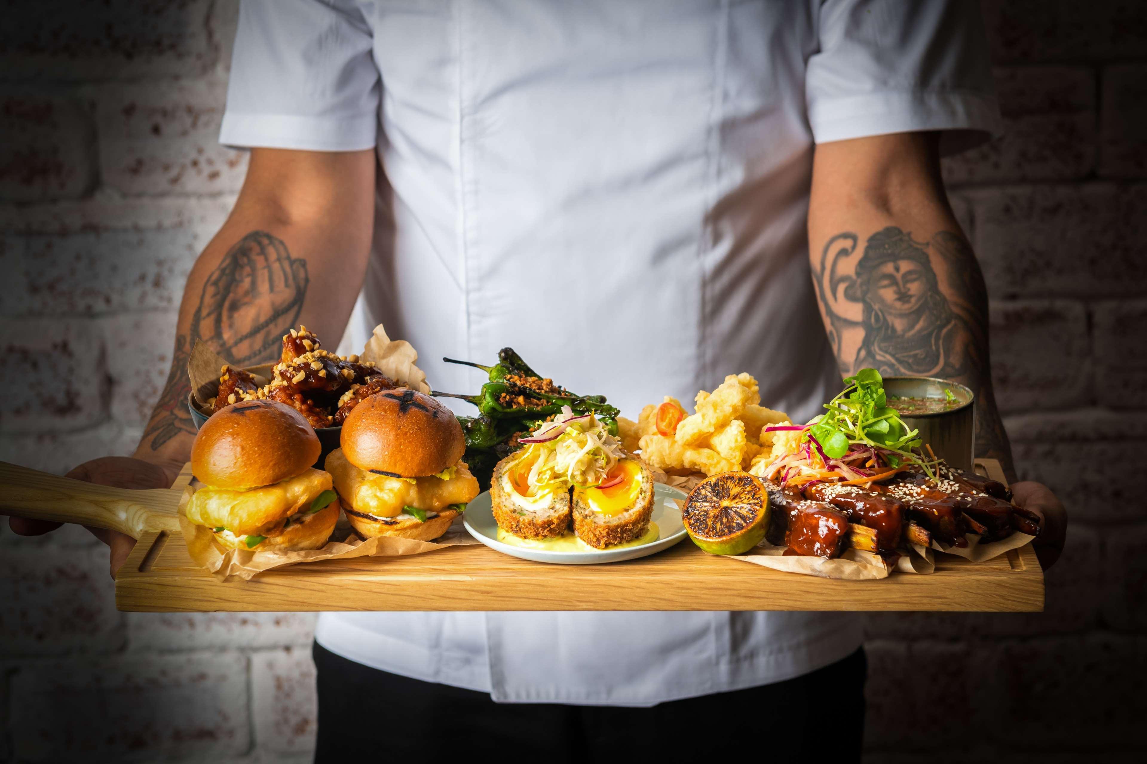 Radisson Blu Hotel, Dubai Canal View Exterior photo The photo shows a wooden platter being held by a person, featuring a variety of food items. On the left, there are three small burgers, likely topped with a sauce or garnish. Next to them, there are some fried items, possibly shrimp or a similar dish