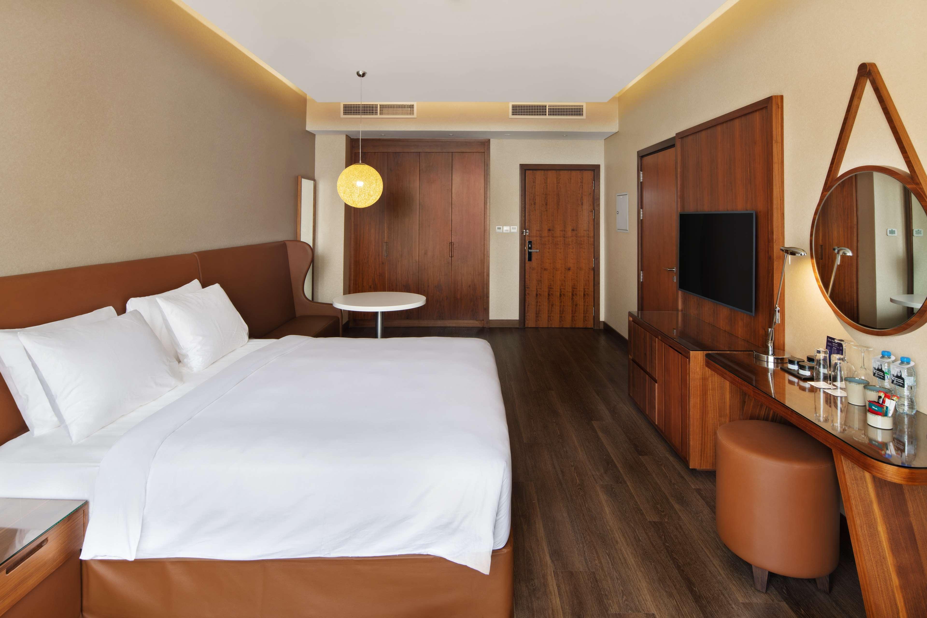 Radisson Blu Hotel, Dubai Canal View Exterior photo The photo shows a modern hotel room with a minimalist design. It features a large bed with white bedding and a brown headboard. To one side, there's a circular table with a single chair, and a warm light fixture hanging above. The walls are painted i