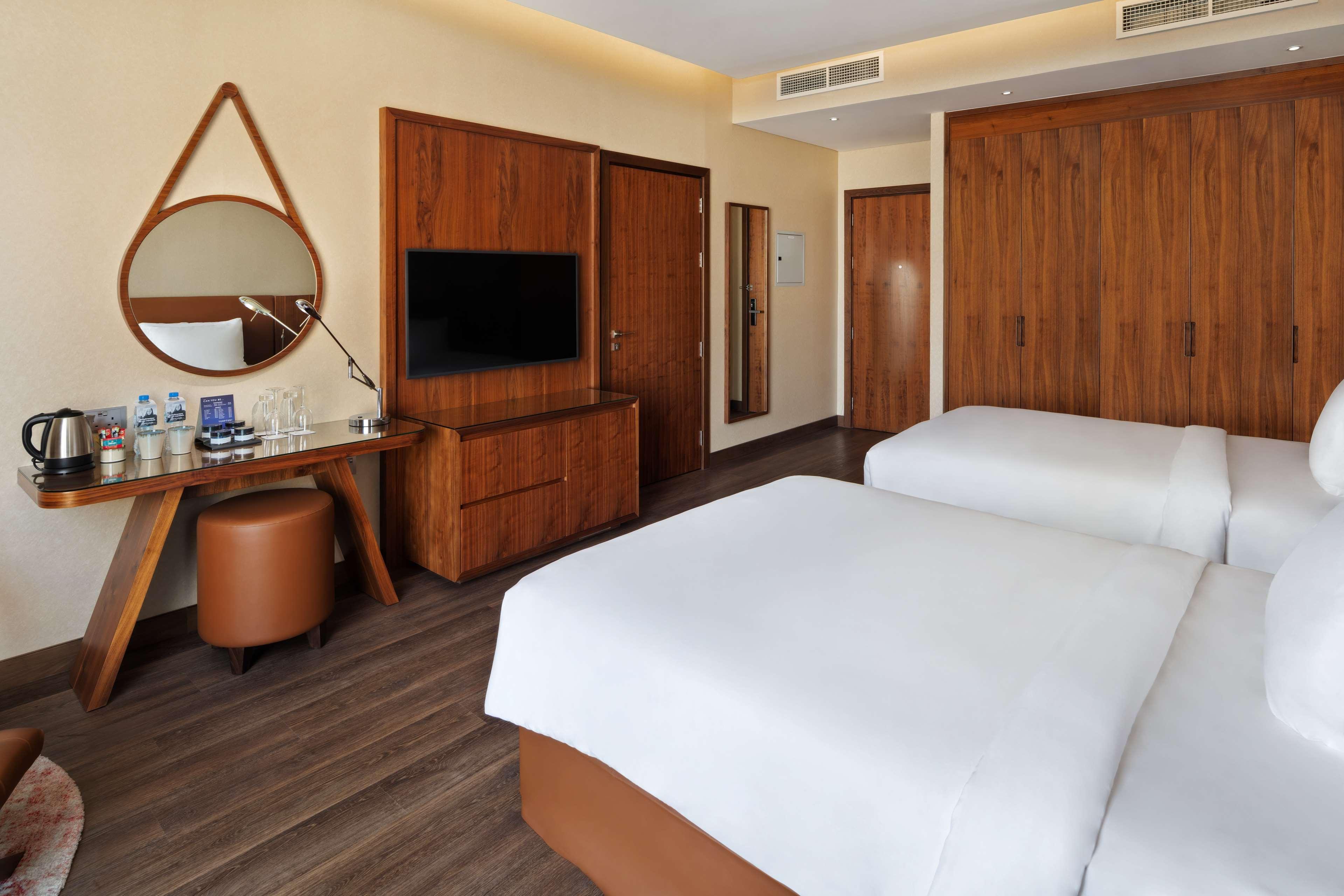 Radisson Blu Hotel, Dubai Canal View Exterior photo The photo shows a modern hotel room featuring two single beds with white bedding. There is a wooden accent wall with a door leading to another space. A large flat-screen TV is mounted on the wall opposite the beds. Next to the beds, there's a stylish