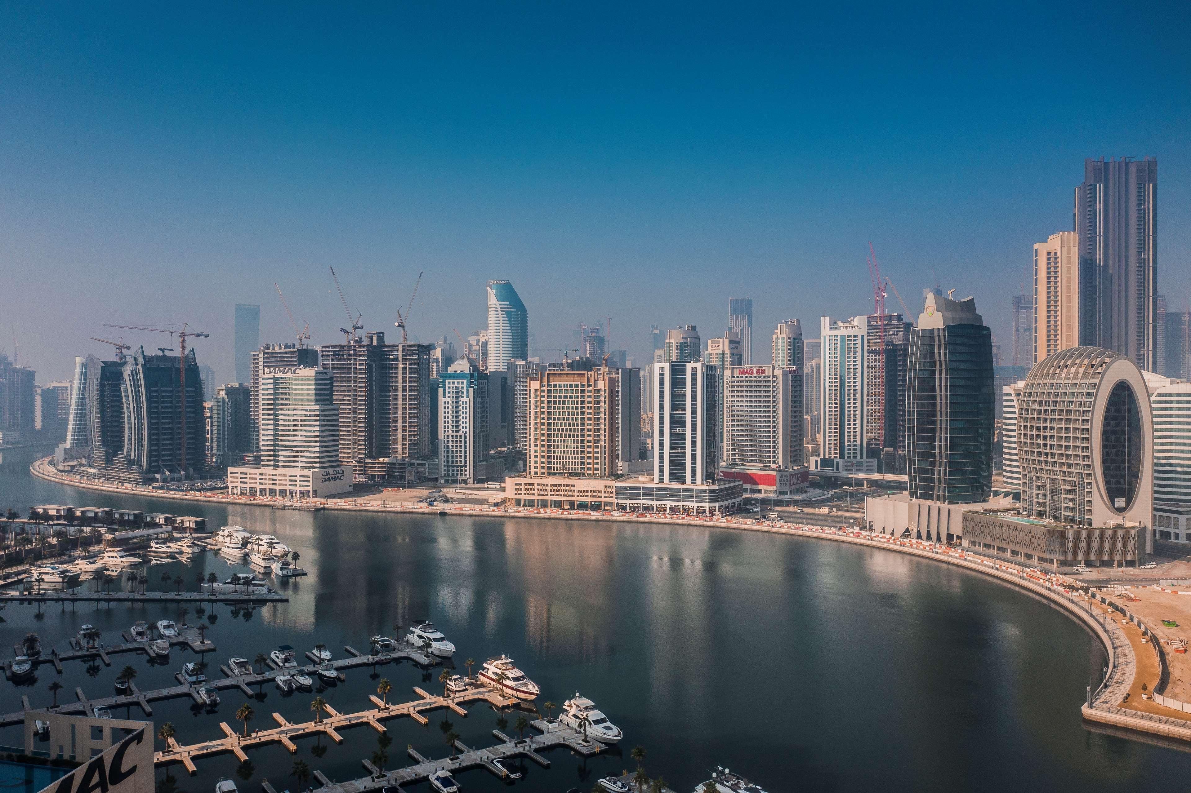 Radisson Blu Hotel, Dubai Canal View Exterior photo The photo showcases a modern city skyline featuring several tall skyscrapers, some of which are under construction. There is a waterfront area with a marina, where numerous boats are docked. The buildings appear to have a mix of architectural styles 