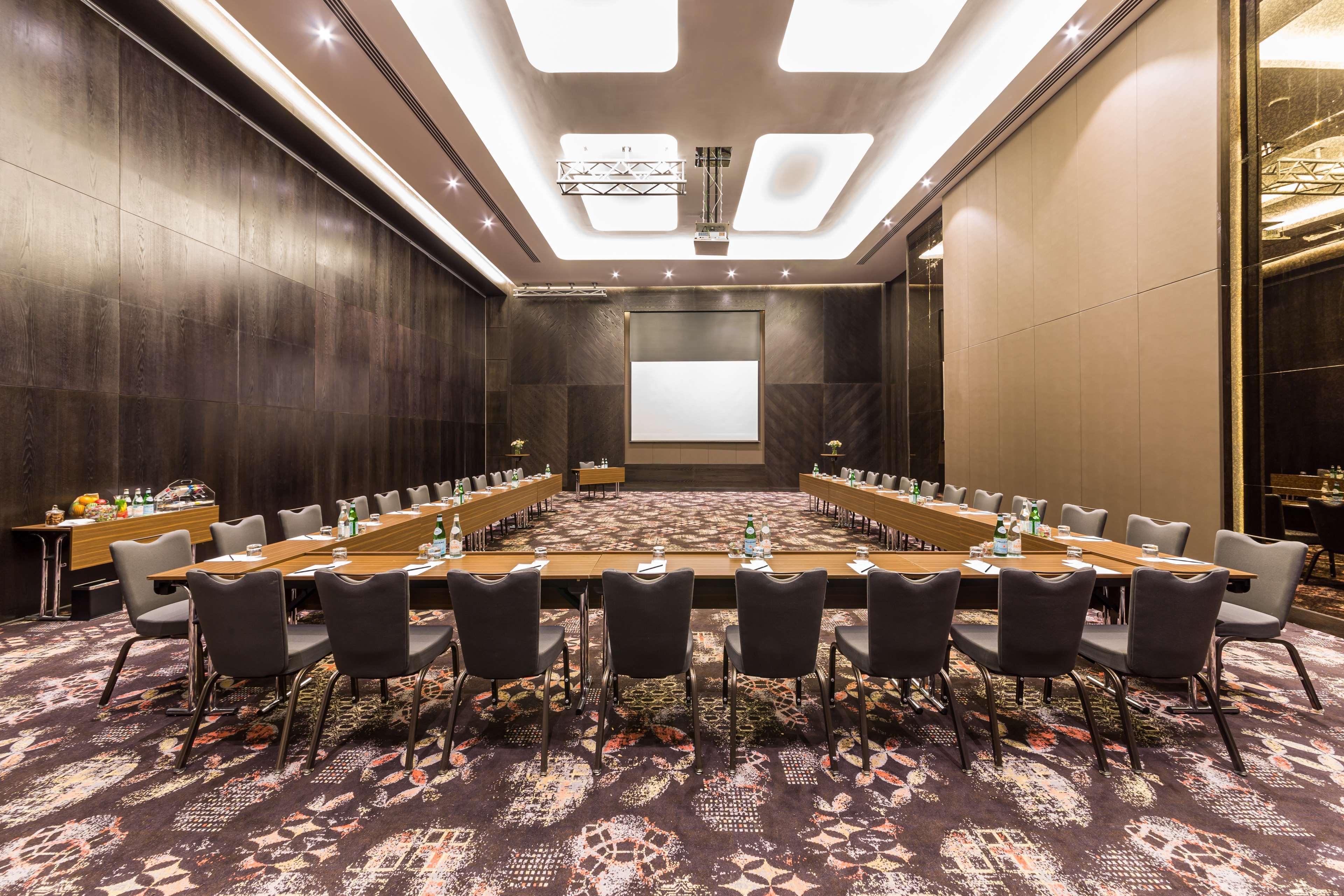 Radisson Blu Hotel, Dubai Canal View Exterior photo The photo shows a conference room set up for a meeting. It features a large rectangular table surrounded by chairs. The room is elegantly decorated, with dark walls and a patterned carpet. There is a projector screen at one end of the room, and sever