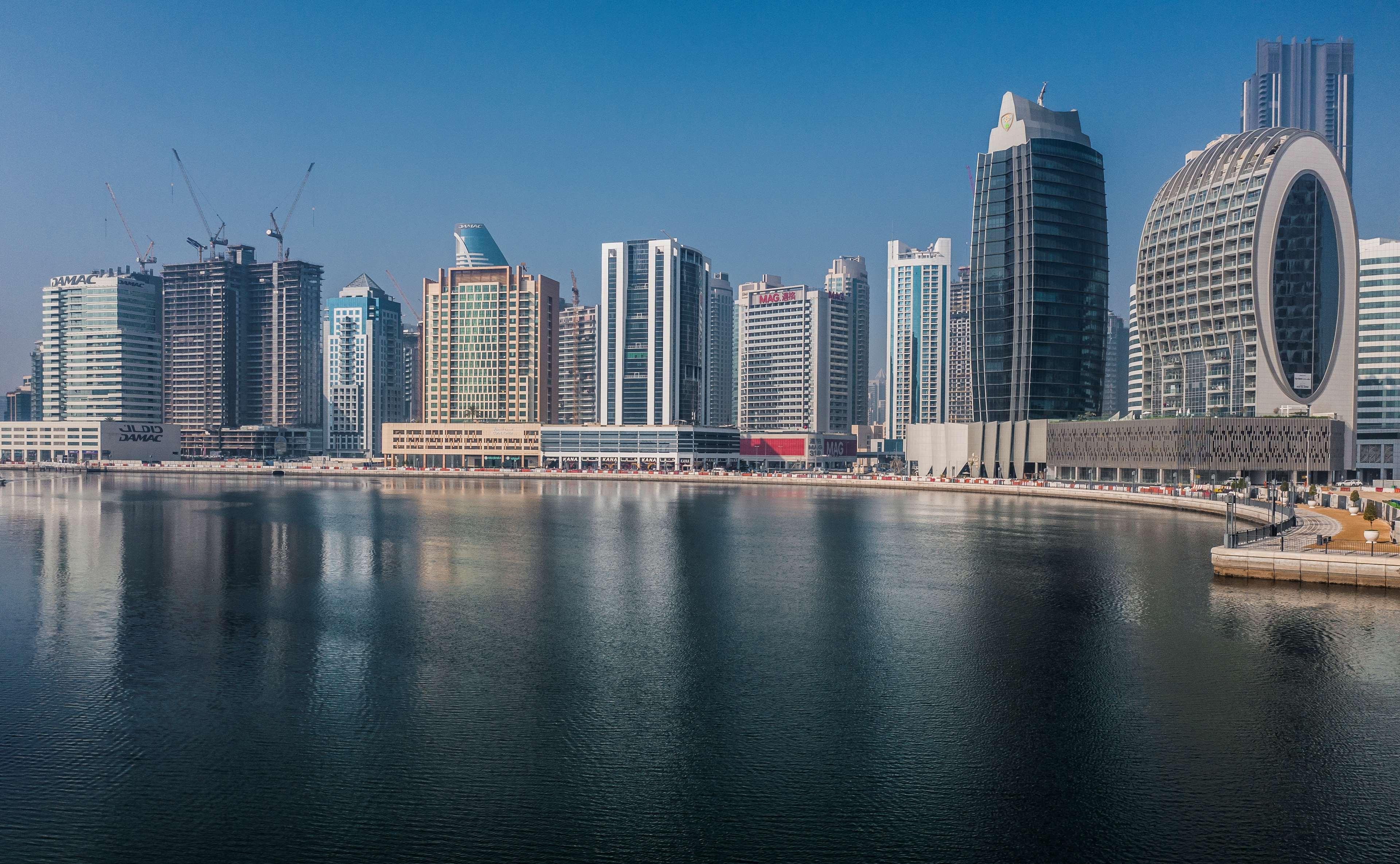 Radisson Blu Hotel, Dubai Canal View Exterior photo The photo depicts a modern skyline featuring a range of tall buildings and skyscrapers beside a body of water. The architecture varies, showcasing a mix of sleek, contemporary designs with glass facades. Some structures seem to be still under constru