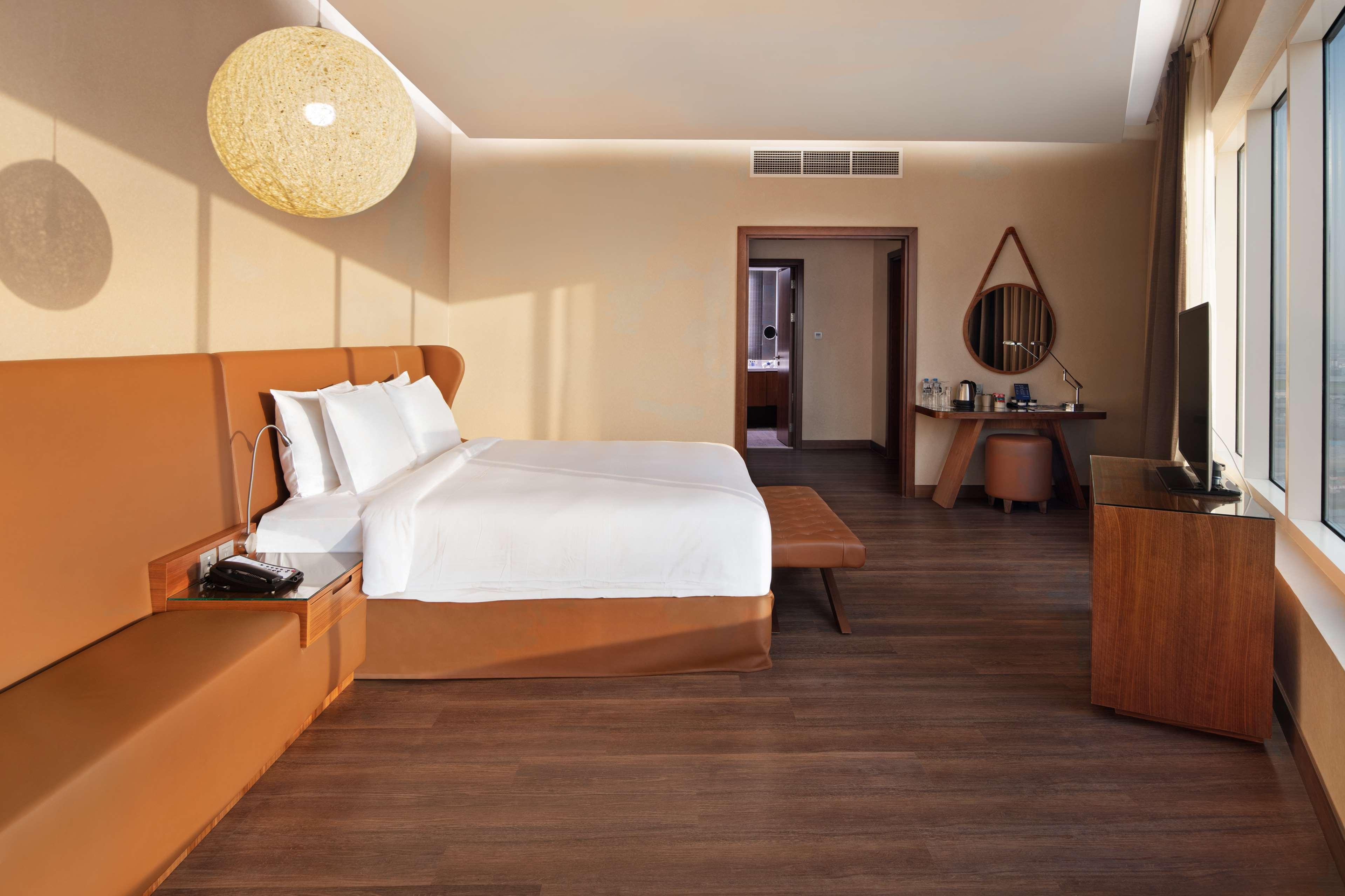 Radisson Blu Hotel, Dubai Canal View Exterior photo The photo shows a modern hotel room featuring a large bed with white bedding, complemented by a brown headboard. To the left, there is a built-in seating area with a matching brown tone. The room has wooden flooring and is decorated in neutral colors