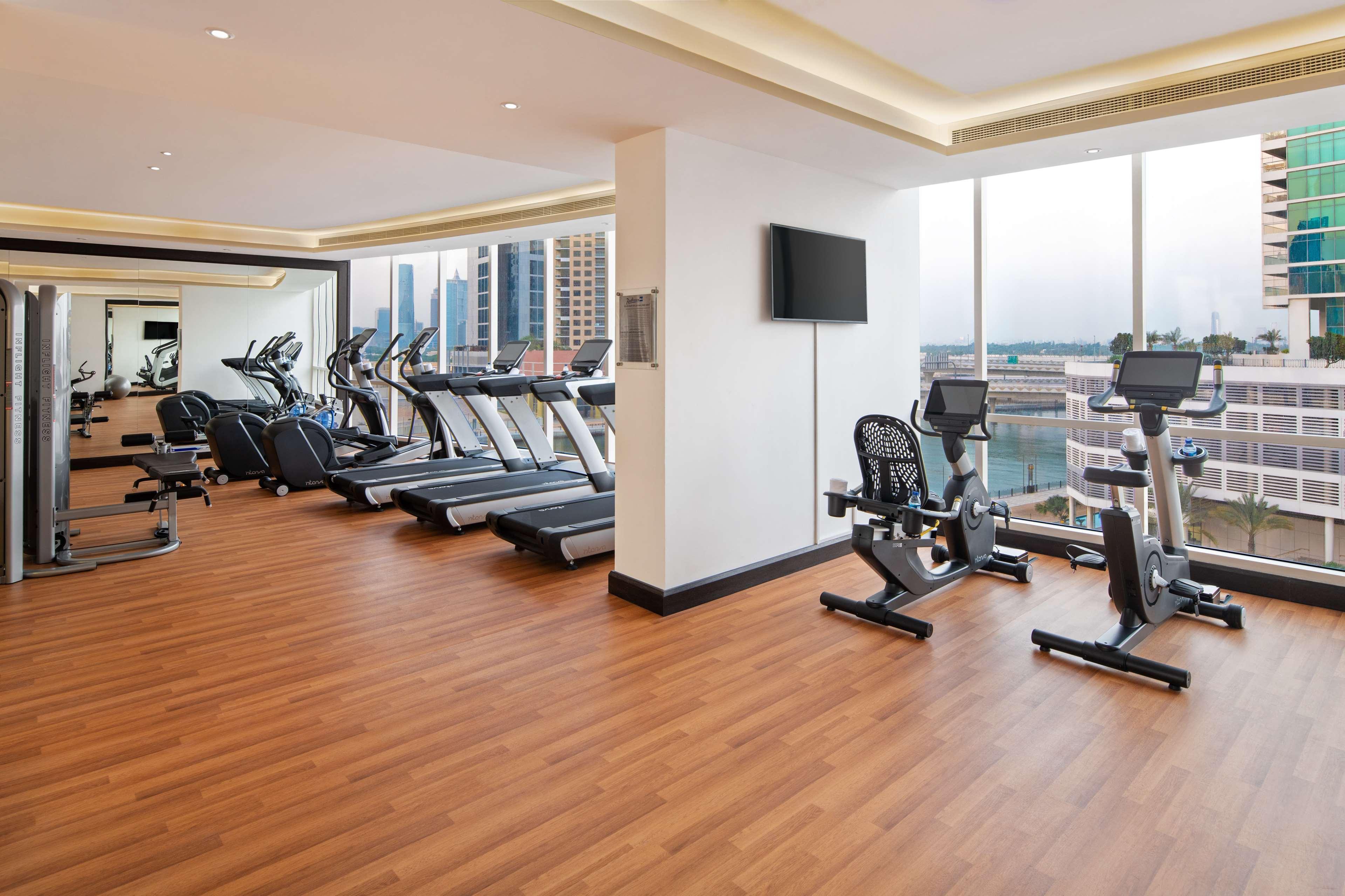 Radisson Blu Hotel, Dubai Canal View Exterior photo The photo shows a modern gym or fitness room with several exercise machines. There are treadmills lined up along one wall, and on the opposite side, there are stationary bikes. The room features large windows that allow natural light to fill the spac