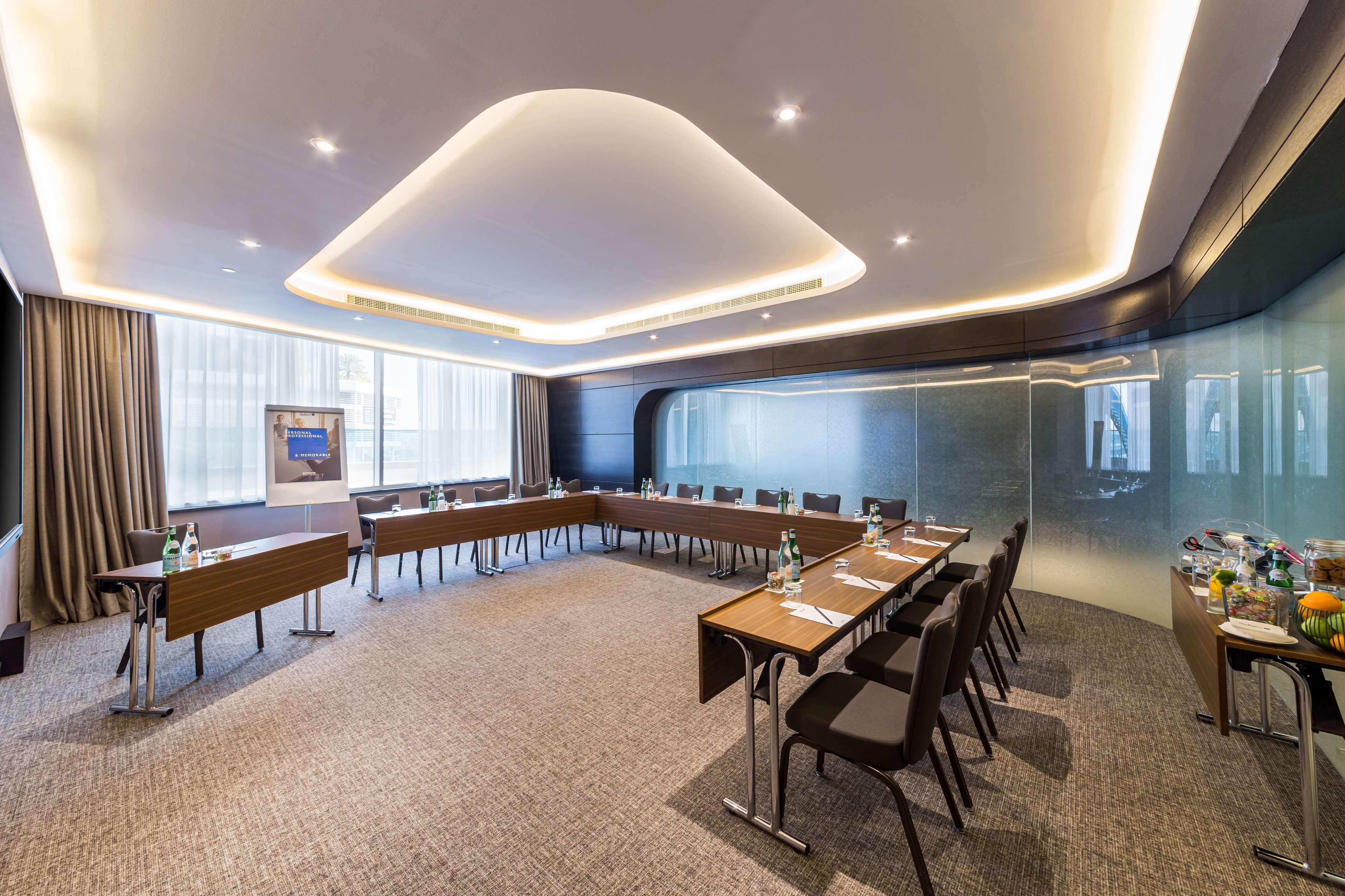 Radisson Blu Hotel, Dubai Canal View Exterior photo The photo shows a modern conference room. It features a large rectangular table surrounded by chairs, with additional chairs arranged along the edges. The room has a sleek design with a subtle color palette, incorporating soft lighting that highlight